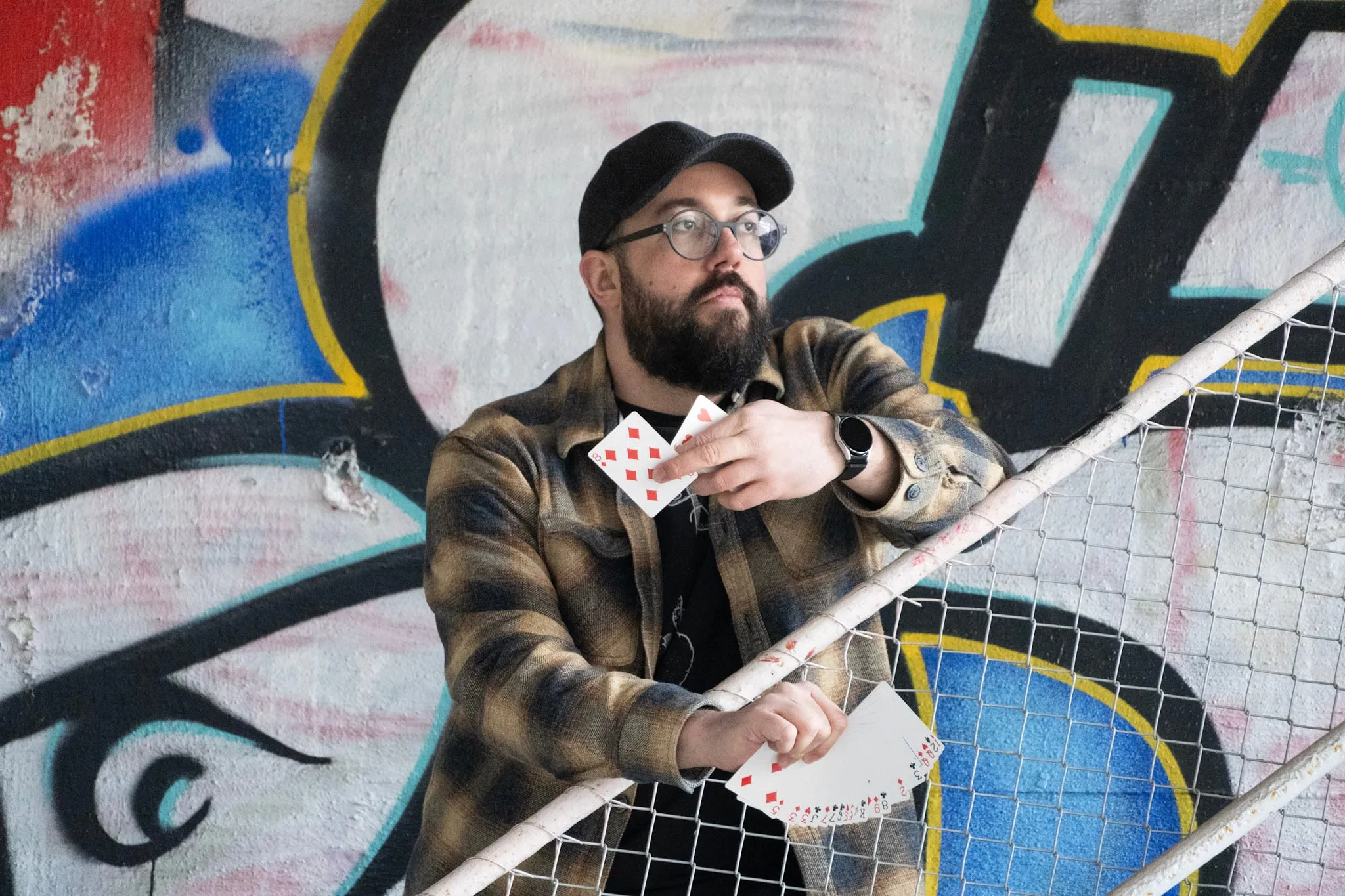 Manuel Kirsch fächert Spielkarten vor einer bunten Graffitiwand.