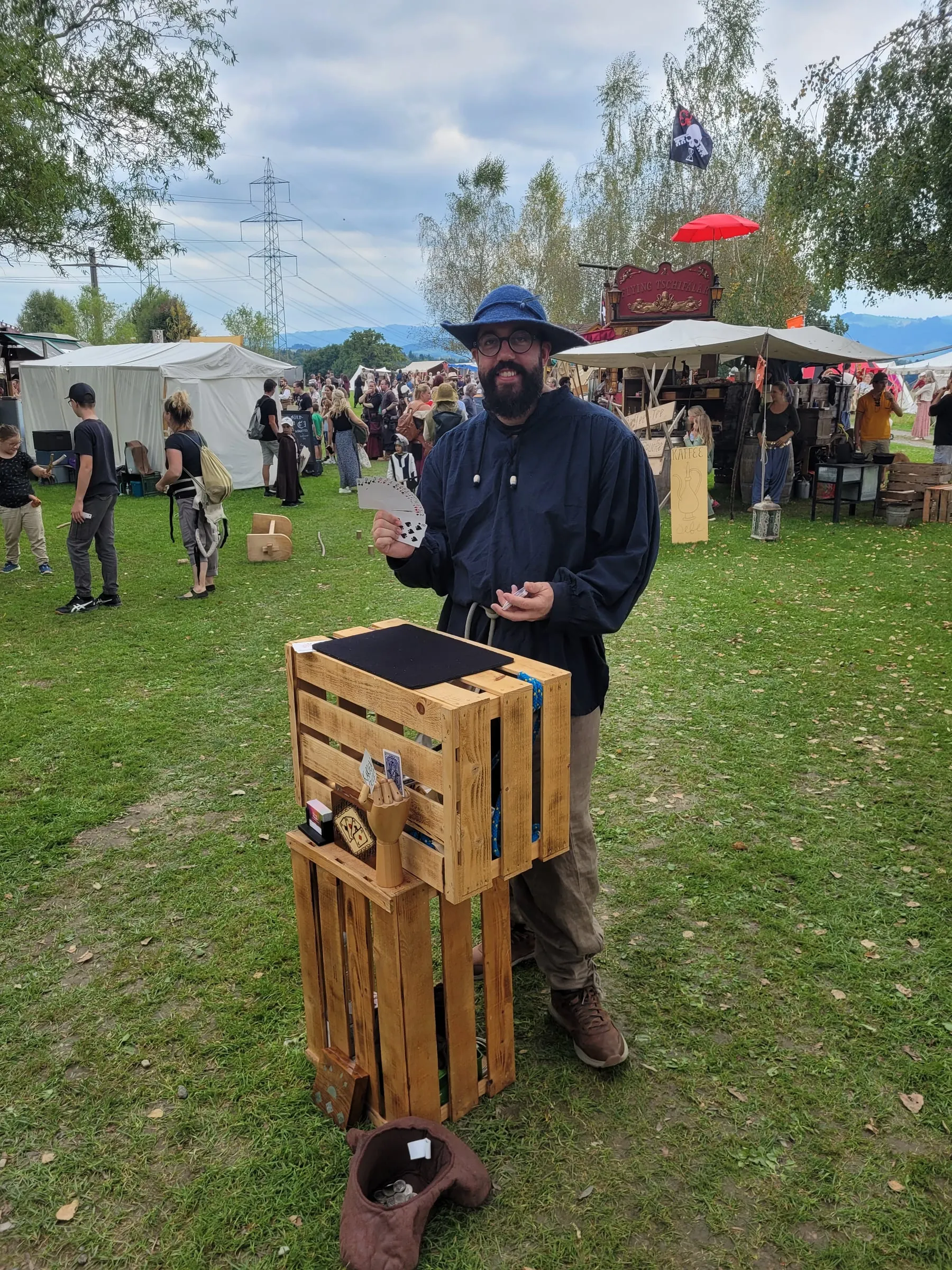 Manuel Kirsch mit Hut zeigt auf der Marktwiese einen Kartentrick an seiner Holzkiste.